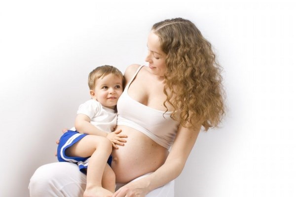 На фото – беременная женщина держит на коленях ребенка